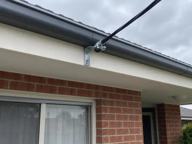 Overhead service cable and bracket on a brick house fascia under a tiled roof in Rutherford